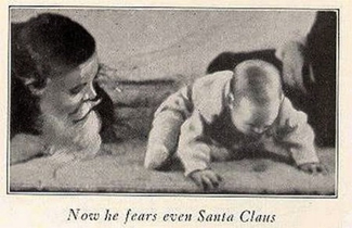 A photograph shows a man wearing a mask with a white beard; his face is close to a baby who is crawling away. A caption reads