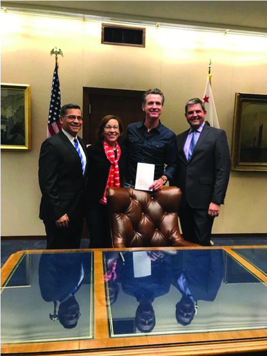 Four people stand behind a desk: (Left to Right) Attorney General Becerra, AARP Advocacy Manager Blanca Castro, Governor News