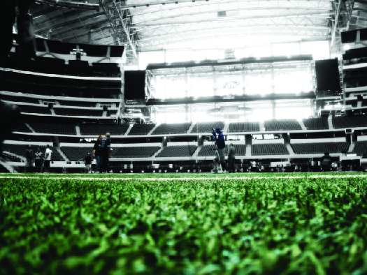 A photo of the inside of a football stadium, showing the field in the foreground and rows of empty seats in the background.