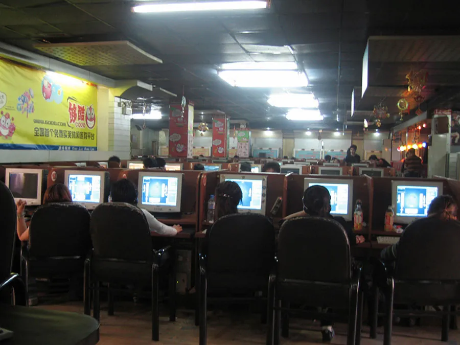 Many people sitting in chairs are shown staring at computer screens in a restaurant/café setting. Chinese posters can also be