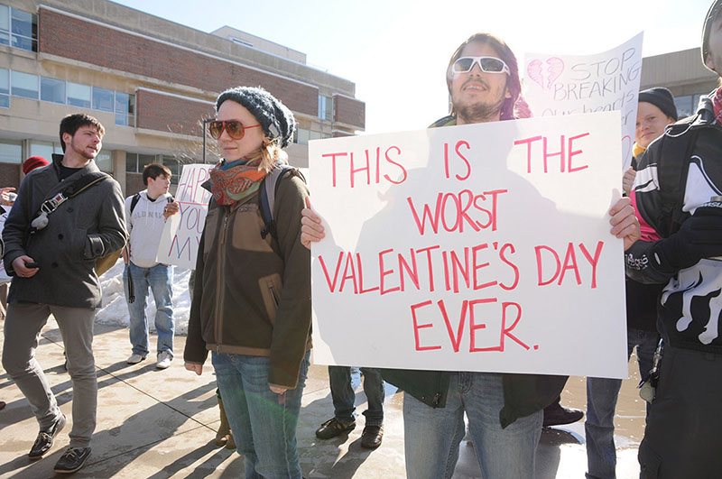 A group of protesters stands together. One holds a sign that reads, "This is the worst Valentine's Day Ever".