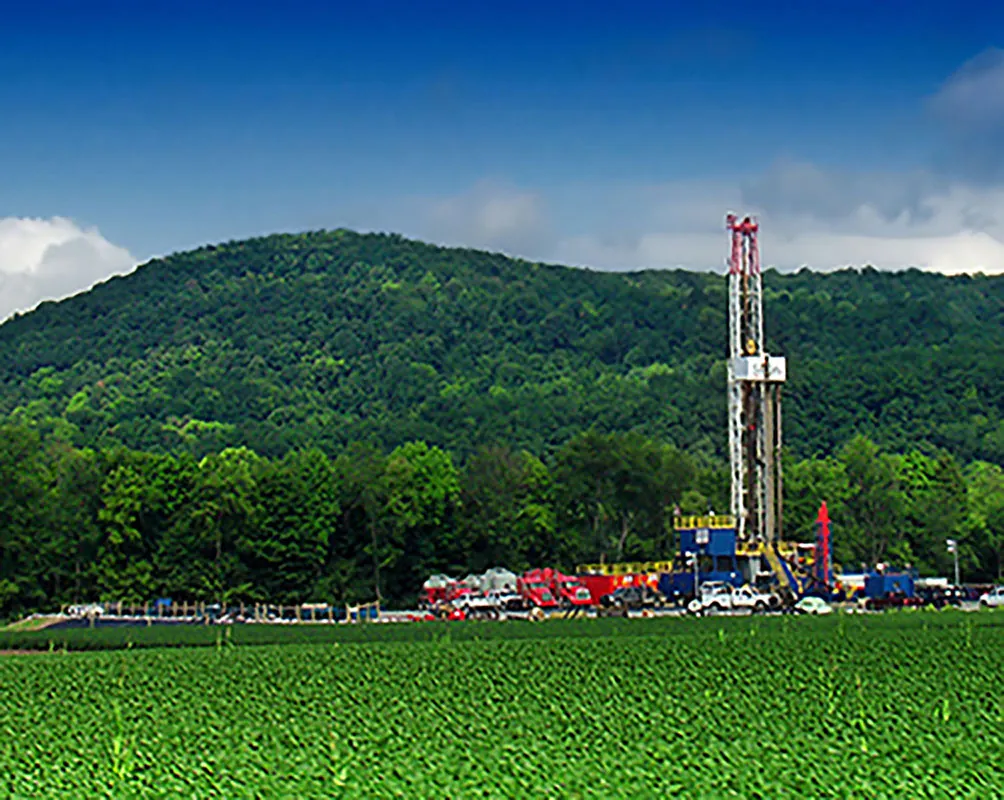 This is a photo of a shale drilling platform below a forested hill.