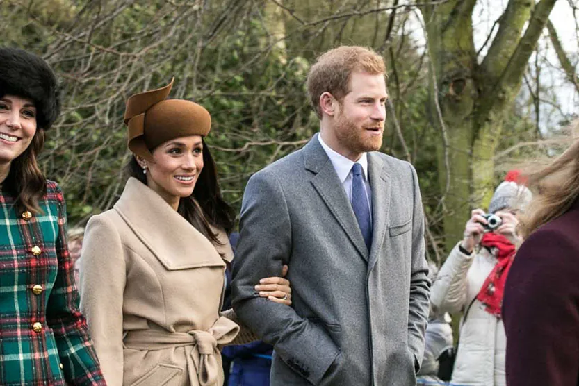 Meghan Markle and Prince Harry stand next to each other with Catherine, Duchess of Cambridge. People take pictures of them.