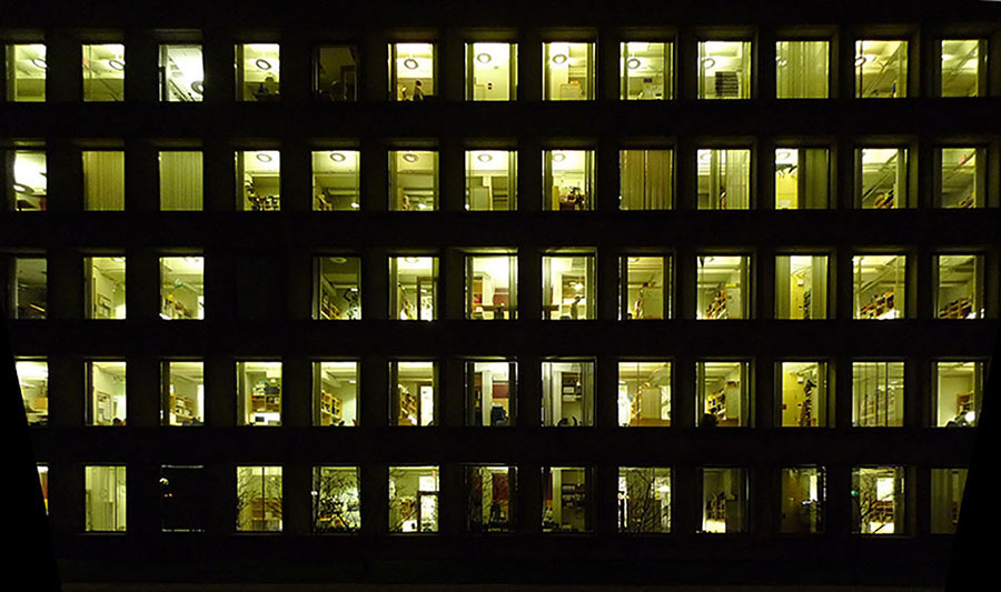 A photo of a large office building at night where you can see many people working inside after hours