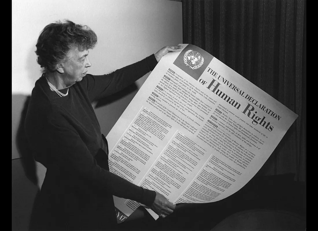 This photograph shows Eleanor Roosevelt holding a large document titled "The Universal Declaration of Human Rights". The logo