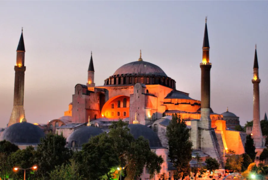 This photograph shows the Hagia Sophia at dusk. It is surrounded by four tall minarets.