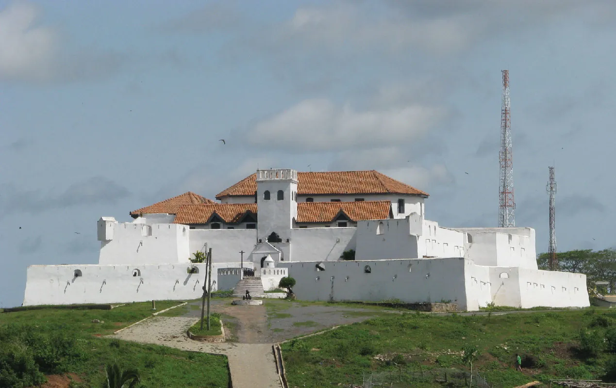 This is a photograph of a four-story castle. The roof is made of orange tiles, the walls are white, and grass is shown in fro