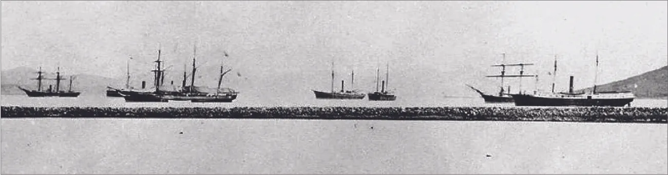 A photograph shows seven ships with tall masts in water. They have black hulls and no sails up. A stone breakwater is shown i