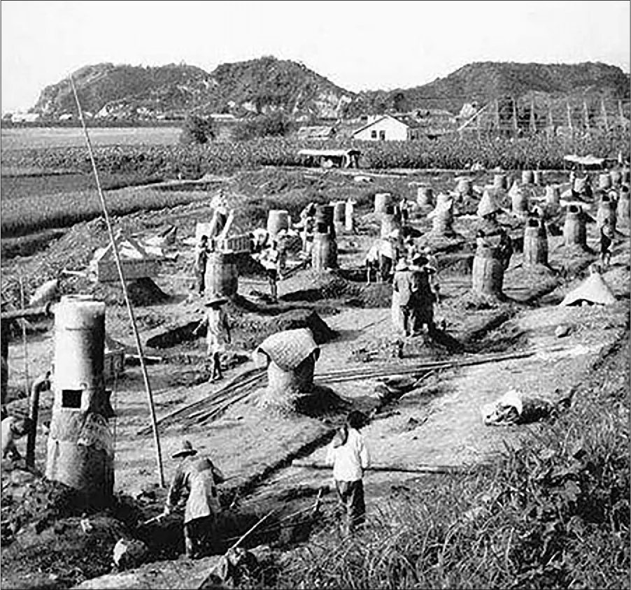 A photograph of a large field is shown with houses and hills in the background. In the foreground workers move about the fiel