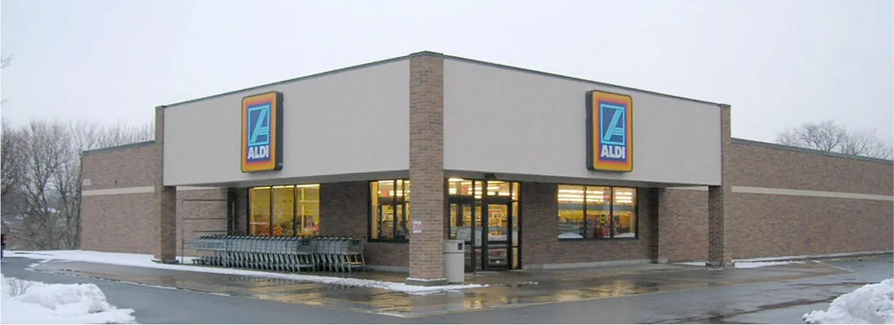 A picture shows the corner of a large, bricked building. The two sides shown are brown bricked with a beige stripe of bricks 